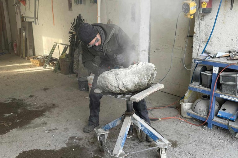 Un tailleur de pierre travaille une pierre avec une meuleuse d'angle dans un atelier