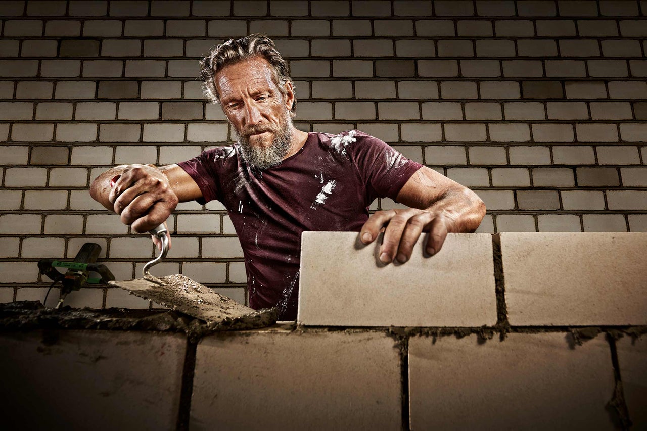 Ein Maurer arbeitet an einer Ziegelmauer mit einer Kelle.