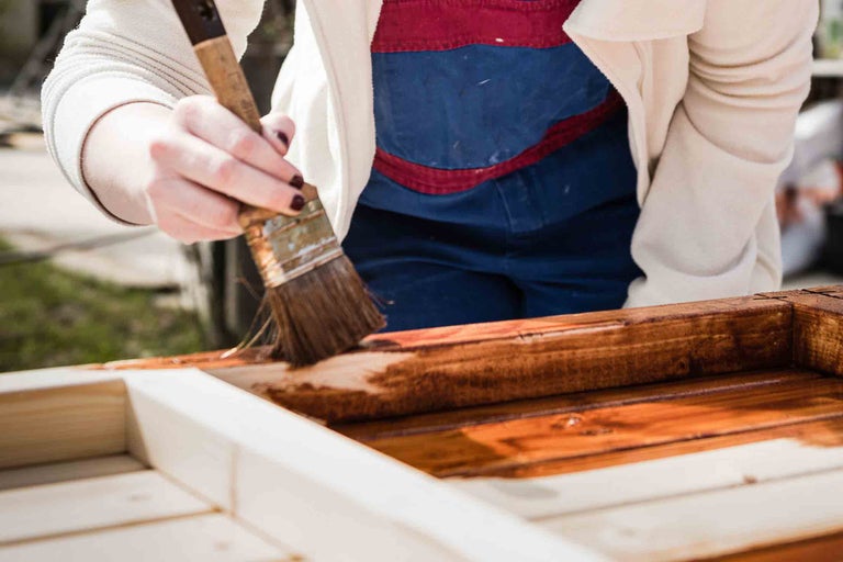 Personne peignant un cadre en bois avec un pinceau et une lasure de protection du bois