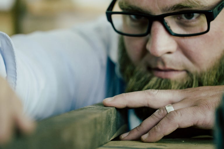 Mann mit Brille und Bart bearbeitet ein Holzbrett