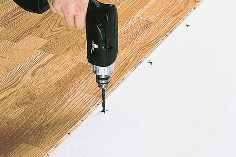 Une perceuse fixe des panneaux de stratifié sur une couche sous-jacente.