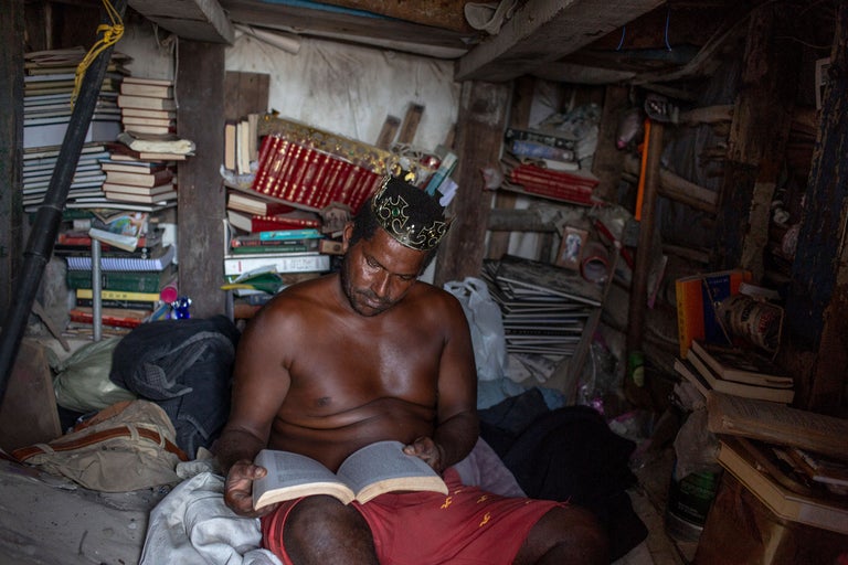 Ein Mann mit Krone liest in einem Raum voller Bücher.