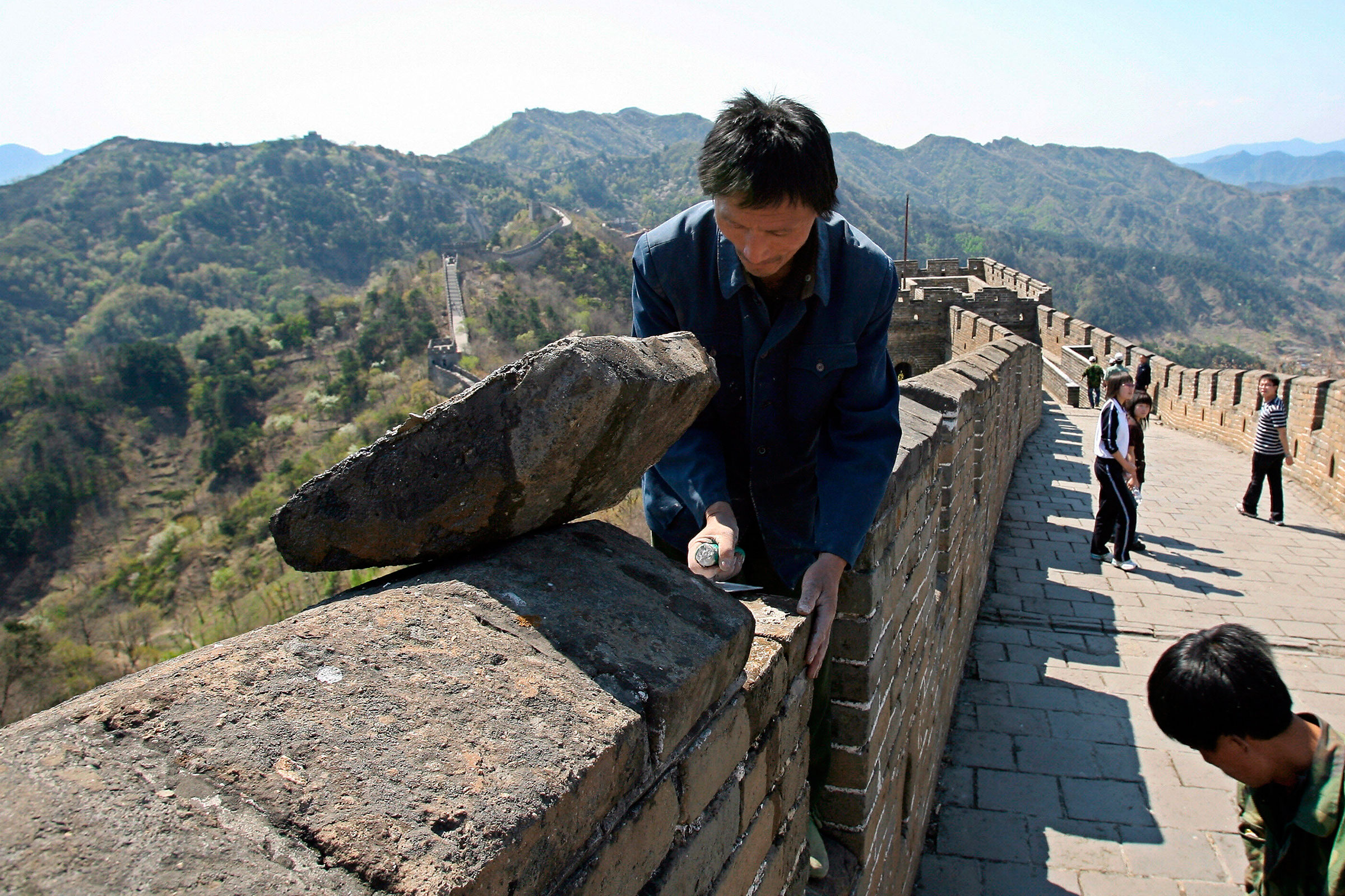 Un homme répare la Grande Muraille de Chine avec de la pierre et des outils.