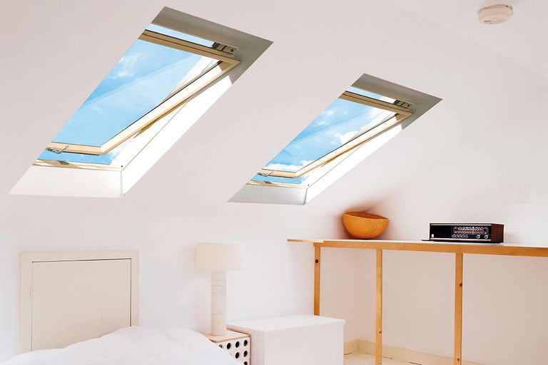 Zwei Dachfenster erhellen einen Dachbodenraum mit Bett und Möbeln.