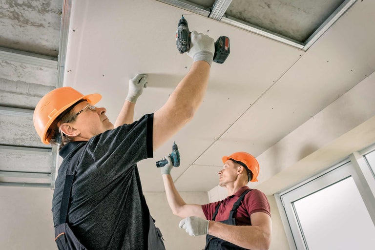 Deux artisans montent un plafond en placoplâtre avec des vis et des visseuses sans fil