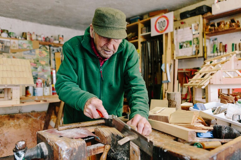 Un homme scie du bois dans un atelier avec des outils et des constructions en bois.