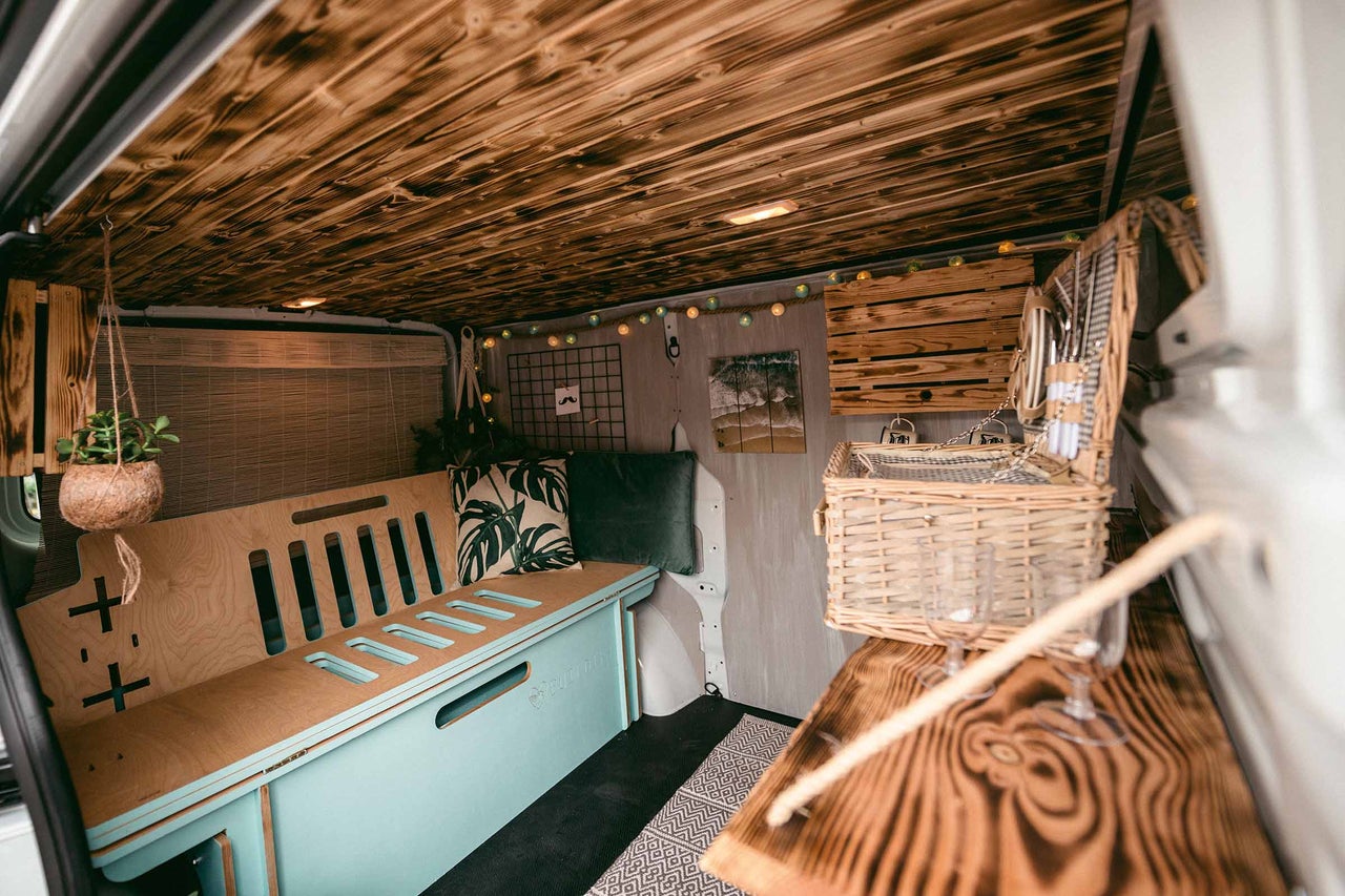 Aménagement intérieur d'une camionnette transformée avec plafond en bois, banquette et panier de pique-nique