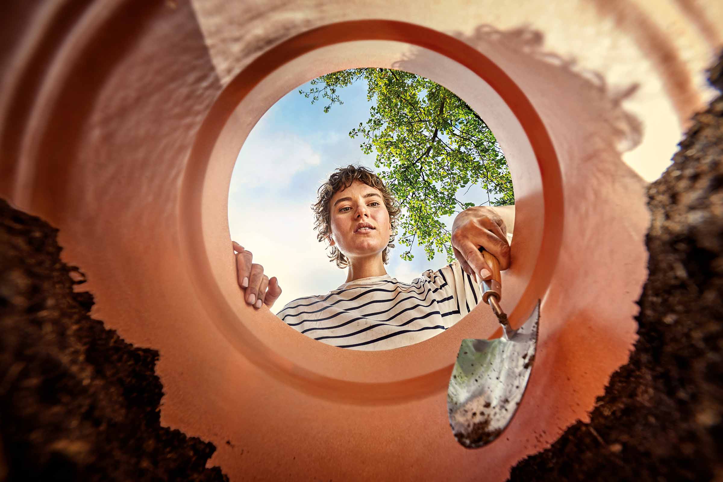 Eine Frau blickt in ein Pflanzgefäß mit einer Schaufel in der Hand.