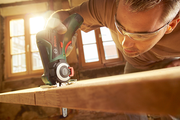 Un homme portant des lunettes de protection travaille une planche de bois avec un outil multifonction Bosch