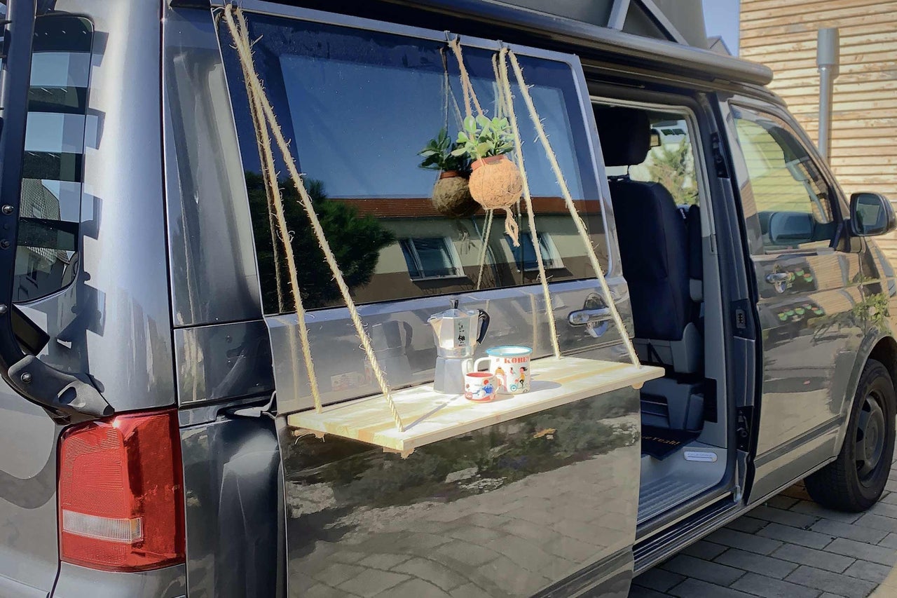 Camping-car avec table suspendue fixée au hayon, avec boissons et plante