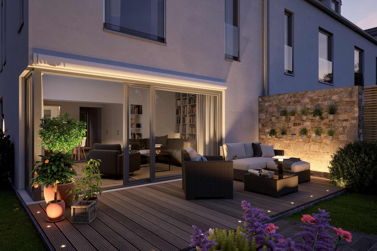 Beleuchtete Terrasse mit Gartenmöbeln, Pflanzen und angrenzendem Haus