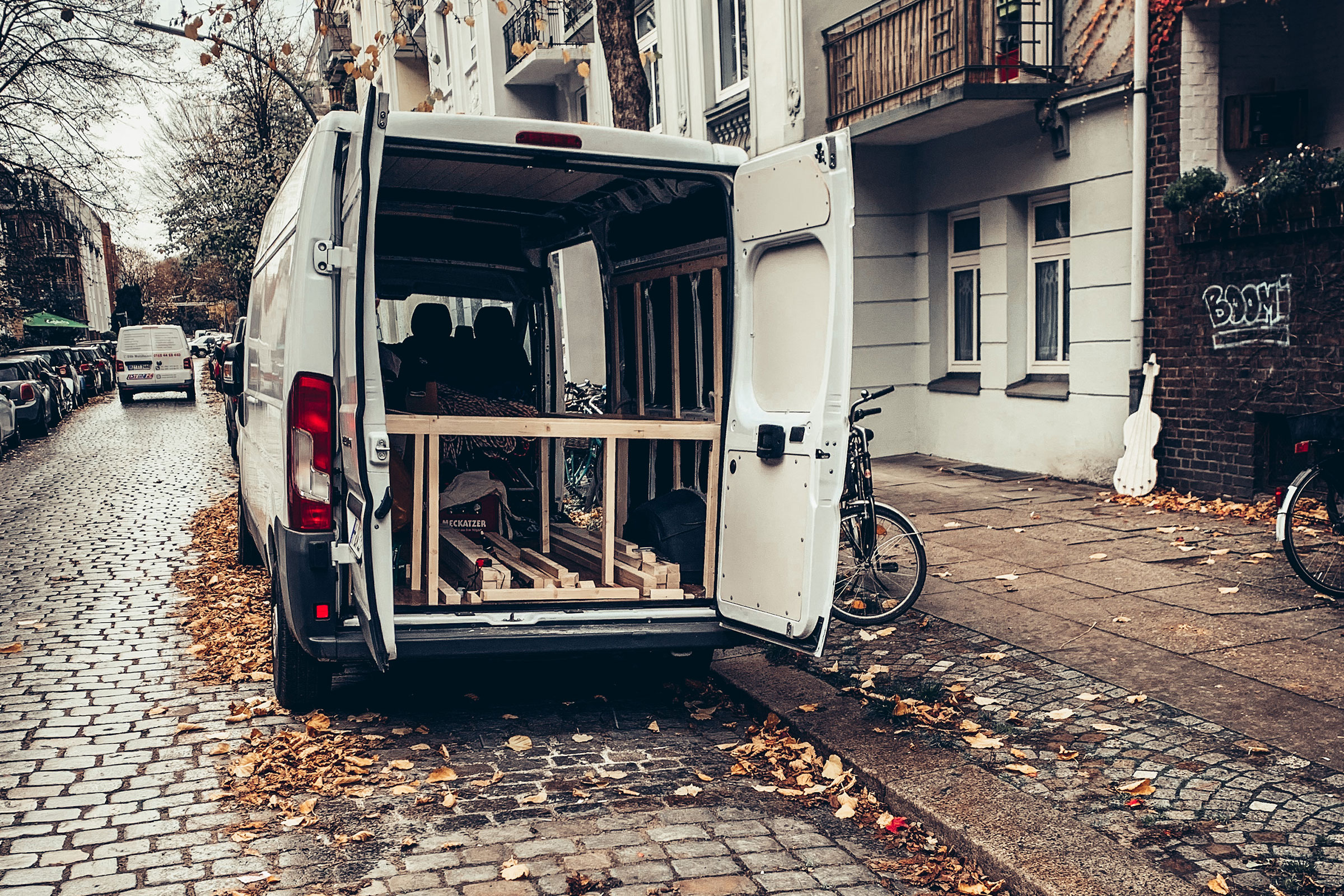 Une camionnette blanche avec portes arrière ouvertes sur une rue pavée et des feuilles d'automne