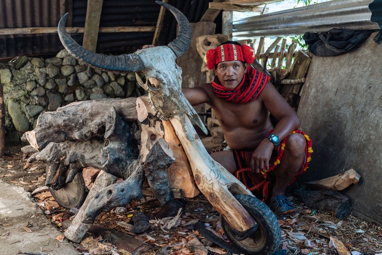 Homme en tenue traditionnelle avec un crâne de buffle sur une moto en bois