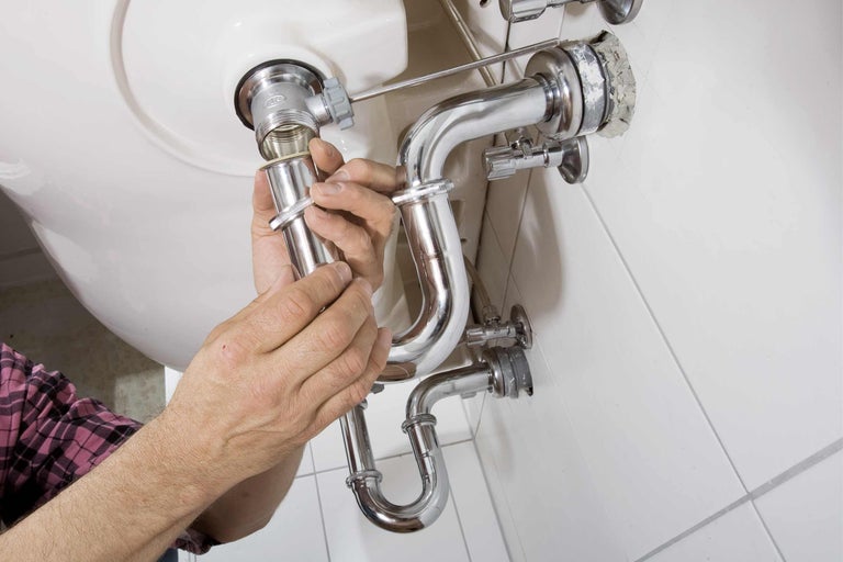 Installation d'un siphon sous un lavabo avec des tuyaux brillants.