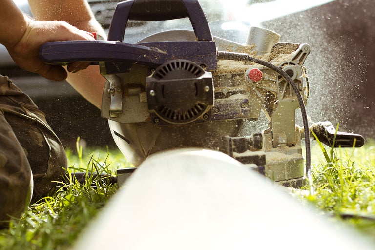 Eine Kapp- und Gehrungssäge schneidet ein Werkstück, mit Holzstaub in der Luft.