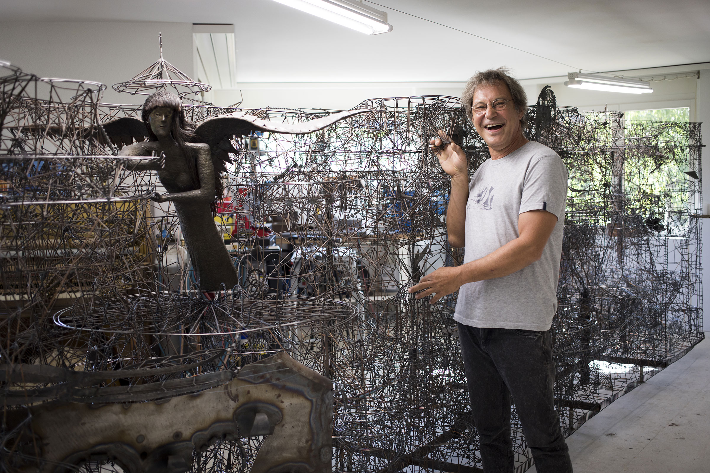 Un homme se tient à côté de sculptures métalliques complexes dans un atelier.