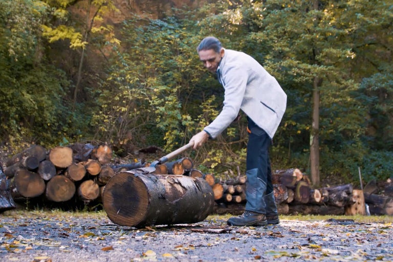 Un homme fend du bois à la hache devant une forêt