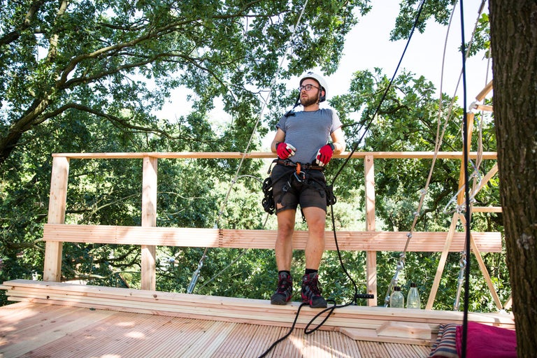 Mann mit Sicherheitsausrüstung auf einer Baumhausplattform mit Holzkonstruktion