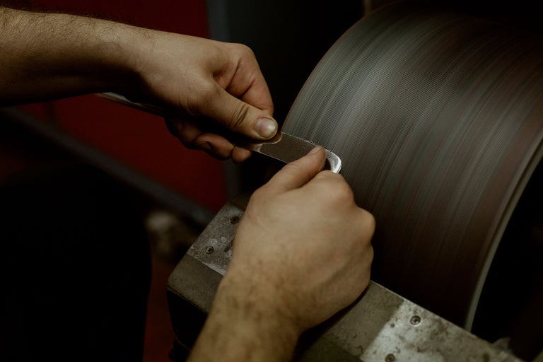 Eine Person schärft ein Werkzeug an einer Schleifscheibe.
