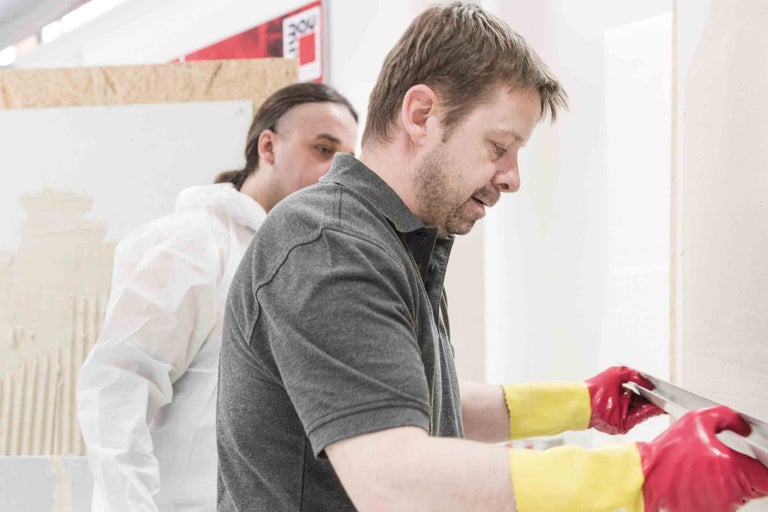 Zwei Handwerker beim Verputzen einer Wand mit einer Glättkelle