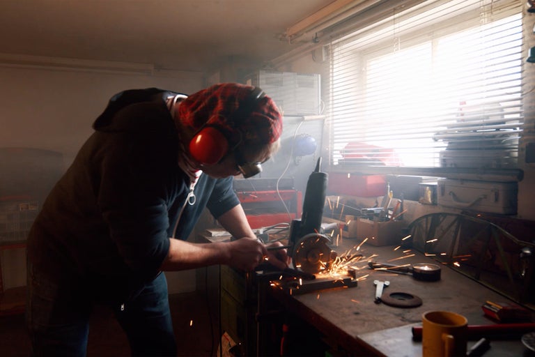 Un homme travaille avec une meuleuse d'angle dans un atelier et porte un équipement de protection.