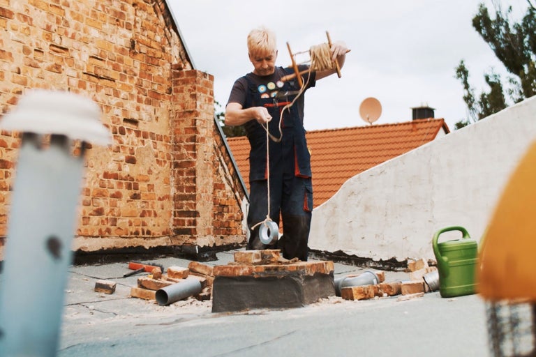 Un artisan travaille sur un toit en briques et utilise des outils ainsi qu'un cordeau tracé lesté de ruban adhésif.