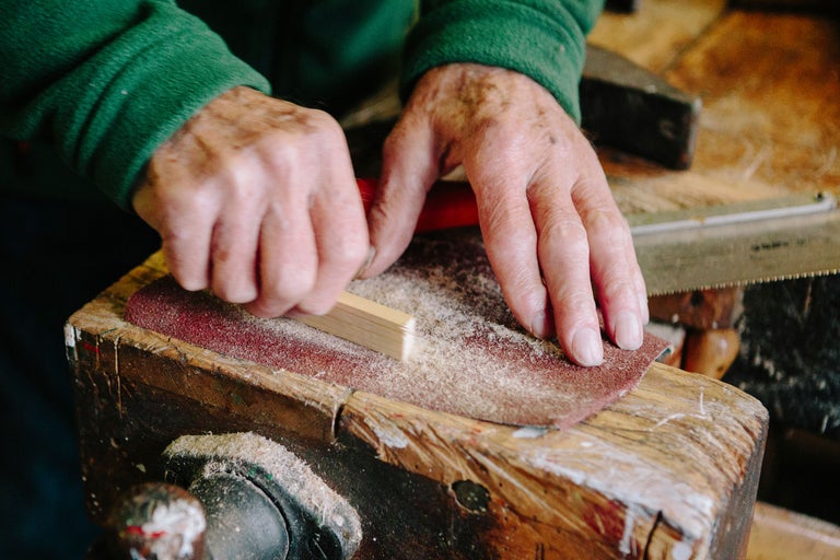 Une personne ponce un morceau de bois avec du papier de verre sur un établi.