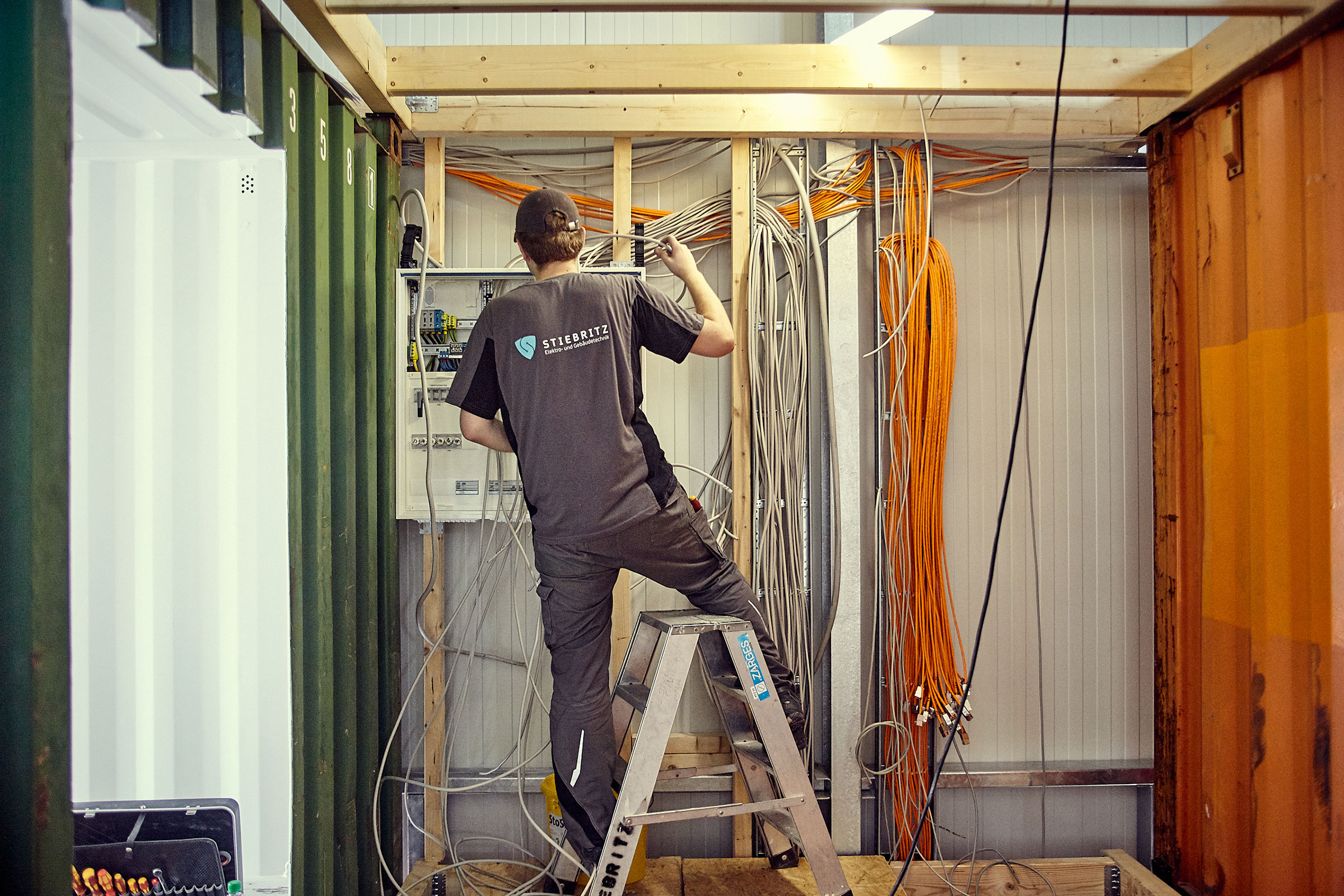 Elektriker auf einer Leiter, der elektrische Leitungen in einem Container installiert