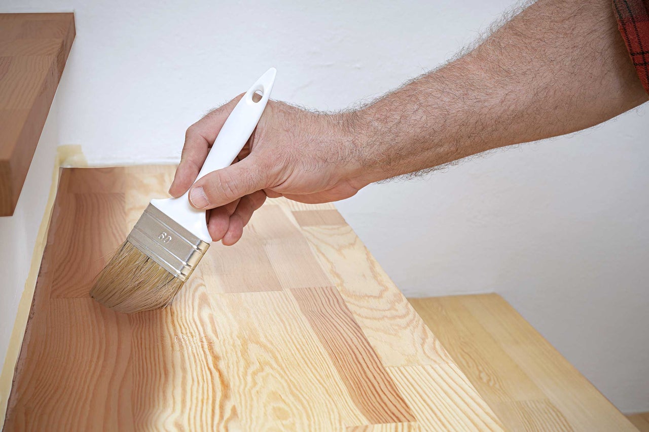 Un artisan vernit un escalier en bois avec un pinceau.