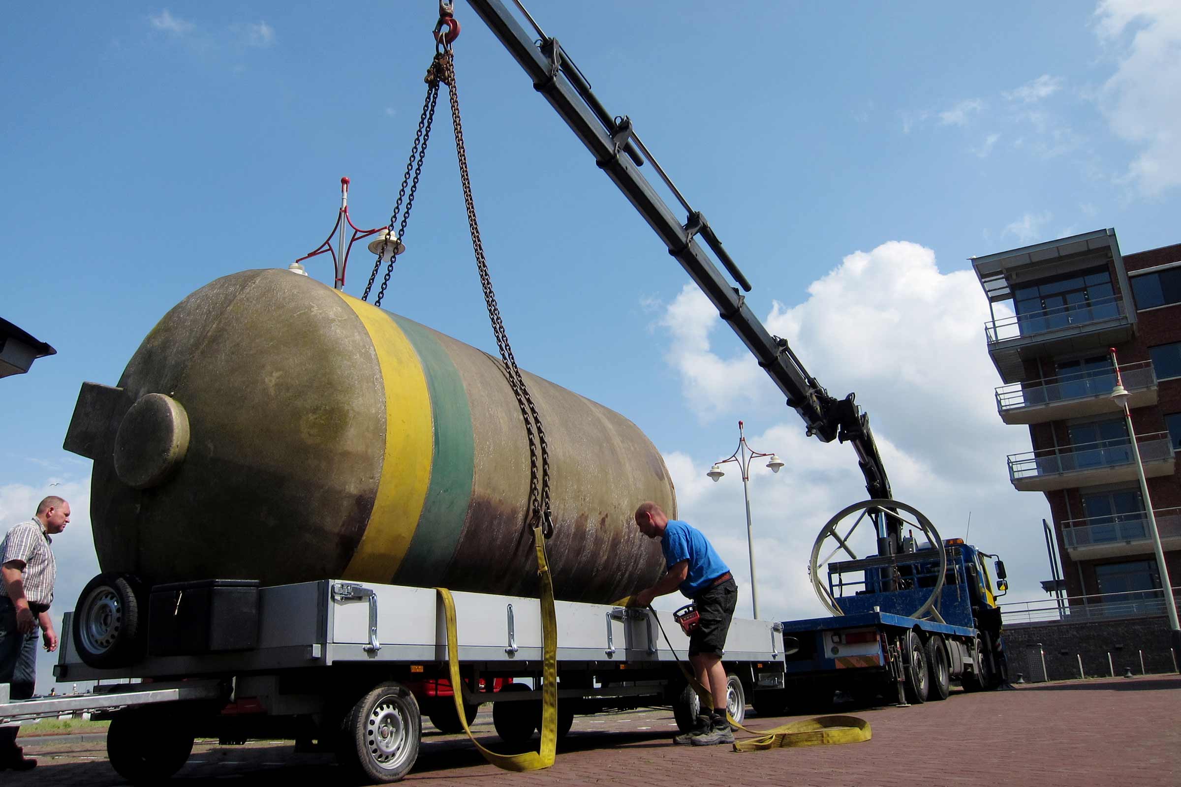 Ein Kran hebt einen großen Tank von einem Anhänger.