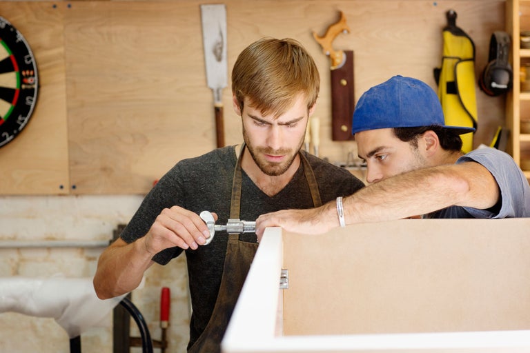 Deux artisans mesurant un cadre en bois avec un pied à coulisse dans un atelier.