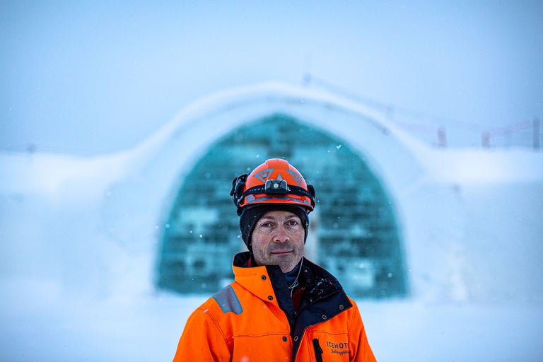 Portrait d'un homme portant une veste orange et un casque devant un bâtiment de glace