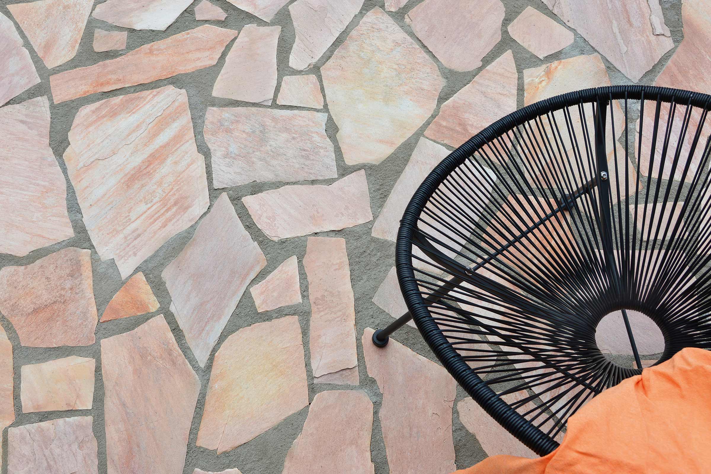 Terrasse avec pavage en pierre naturelle et une chaise en rotin.