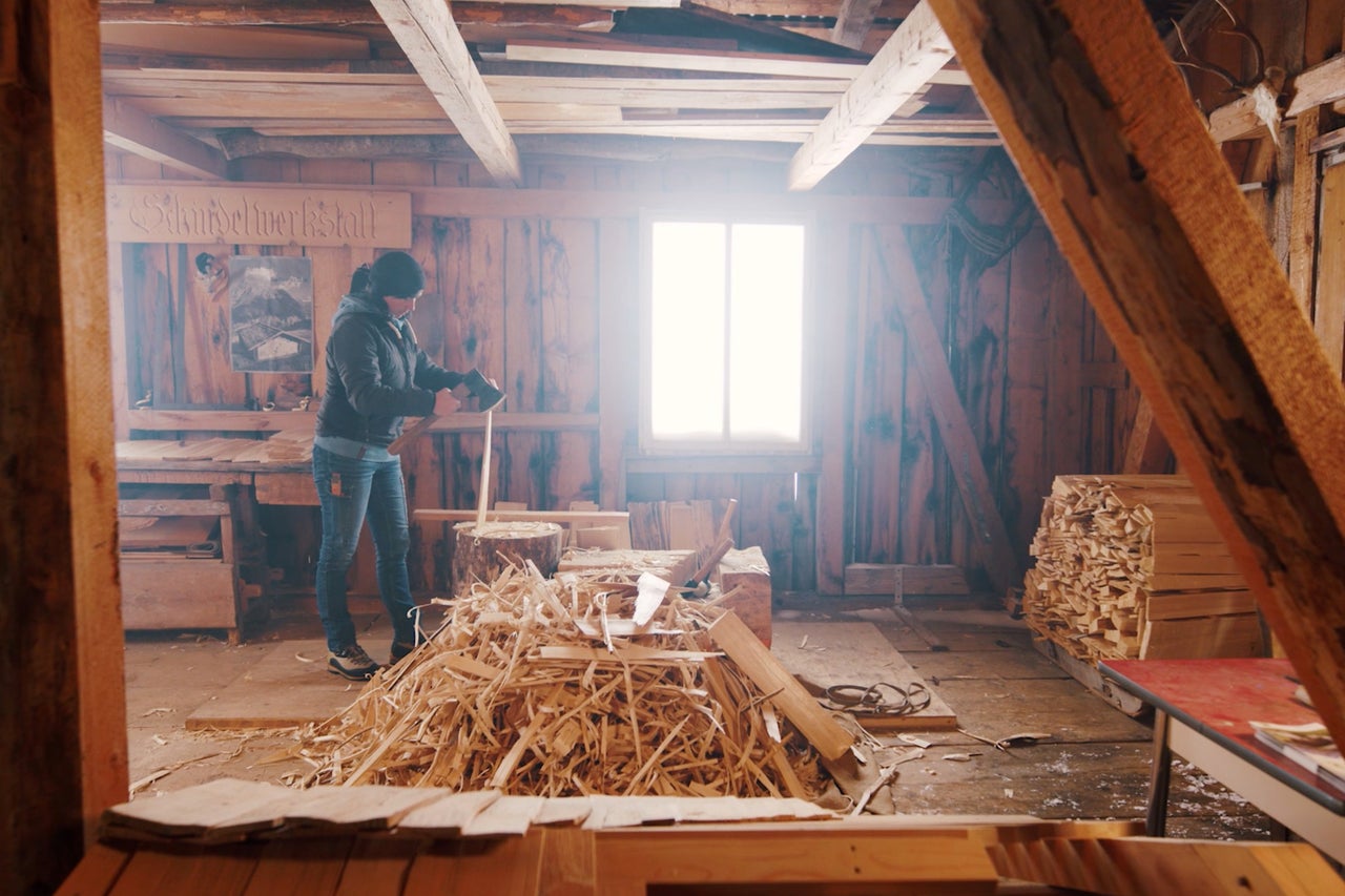 Holzwerkstatt mit Holzstapeln, Holzspänen und einer Person bei der Arbeit