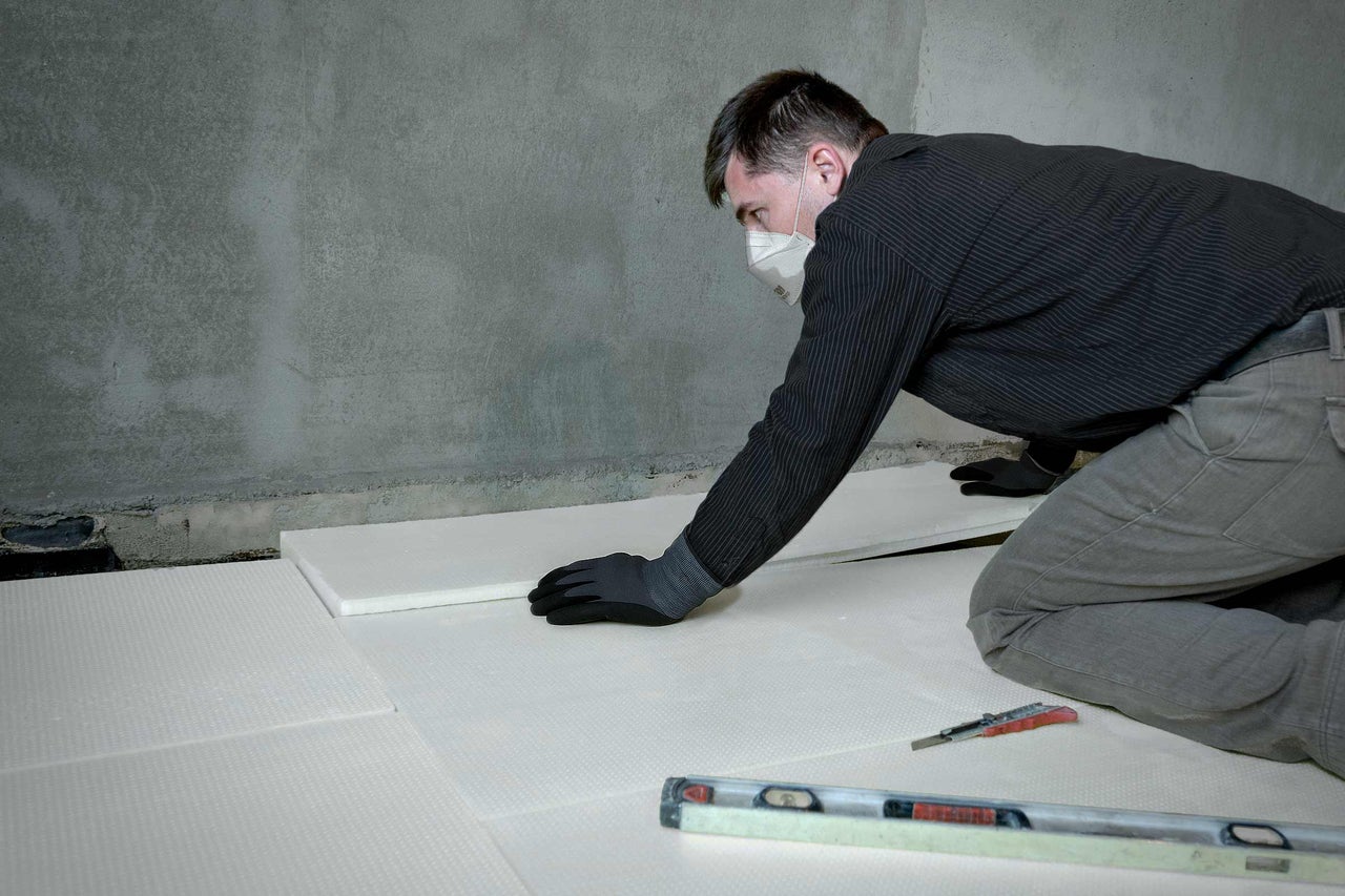 Ein Mann verlegt Dämmplatten auf einem Boden, um die Wärmedämmung zu verbessern.