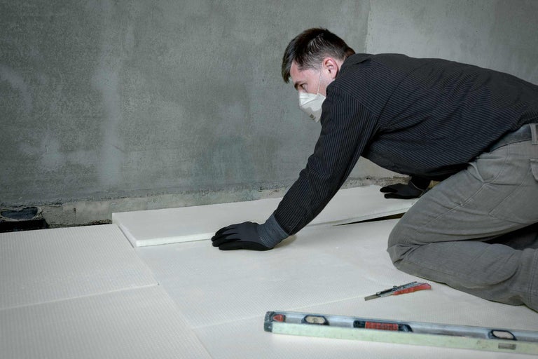 Ein Mann verlegt Dämmplatten auf einem Boden, um die Wärmedämmung zu verbessern.