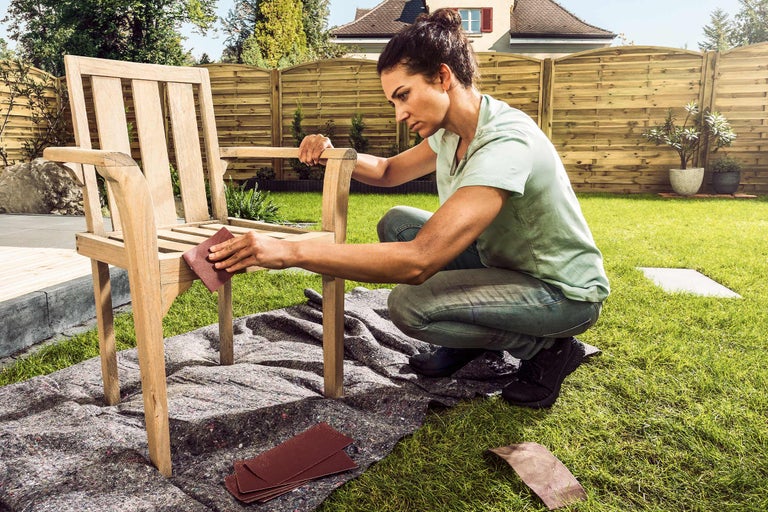 Femme ponçant une chaise en bois dans le jardin avec du papier de verre