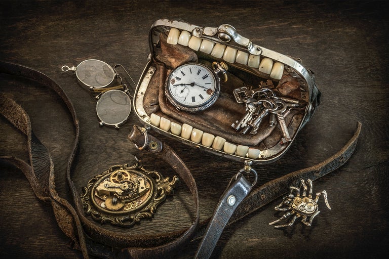 Stillleben mit Gebiss, Taschenuhr, Schlüsseln, Brille, Zahnradanhänger und Lederband auf einer dunklen Holzoberfläche