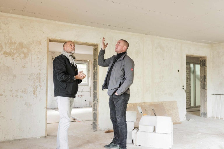 Zwei Männer begutachten eine Baustelle mit Trockenbauwänden und Ziegelsteinen.