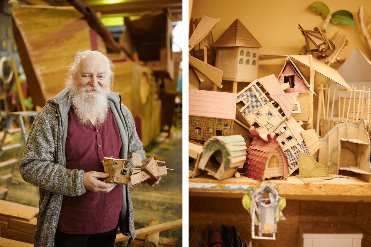 Mann mit Bart präsentiert ein Modellhaus aus Pappe, dahinter weitere Papphäuser