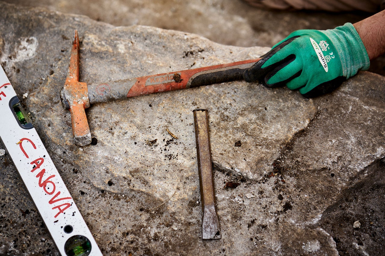 Outils sur plaque de pierre : pic, ciseau, niveau à bulle et gant de travail.