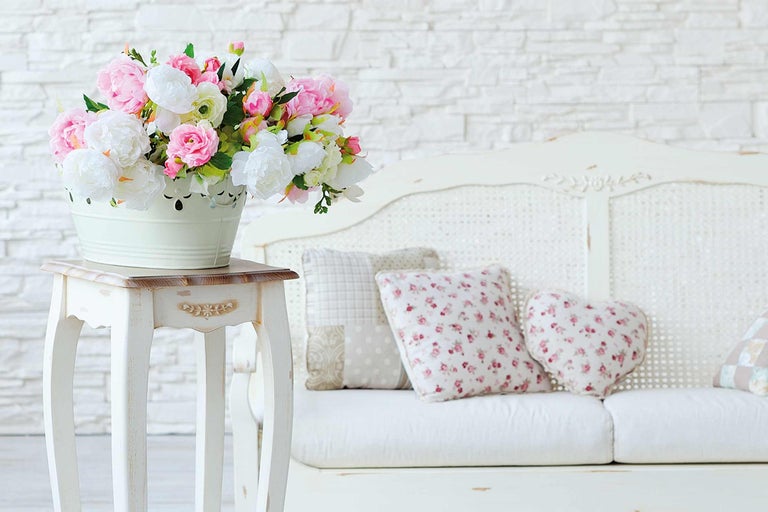 Scène décorative avec un bouquet de fleurs dans un seau sur une table d'appoint à côté d'un canapé avec des coussins
