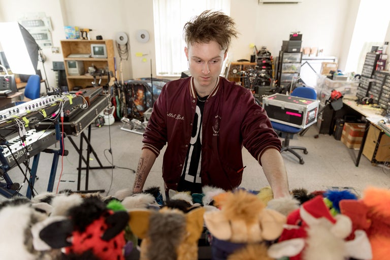 Scène d'un studio de musique avec des instruments de musique électroniques et une personne debout devant une collection de poupées en fourrure.
