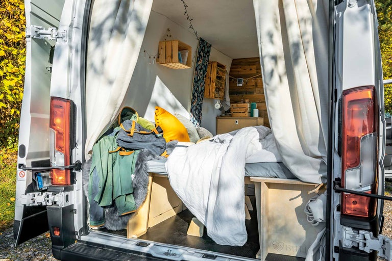 Intérieur d'un van aménagé avec lit, étagères et vêtements