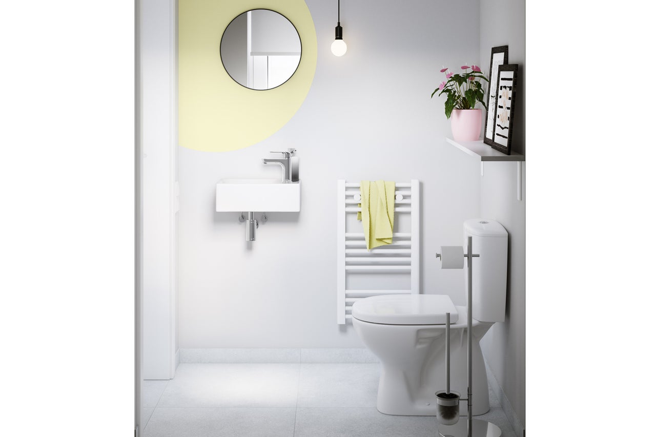 WC visiteurs moderne et lumineux avec petit lavabo mural, miroir rond, radiateur sèche-serviettes blanc et WC au sol.