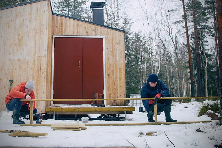 Zwei Personen bauen eine Holzveranda vor einem Holzhaus im Winter.