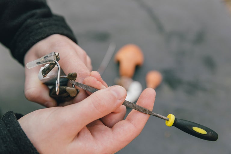 Detailaufnahme von Händen, die mit einer Schlüsselfeile an einer Angelrolle arbeiten