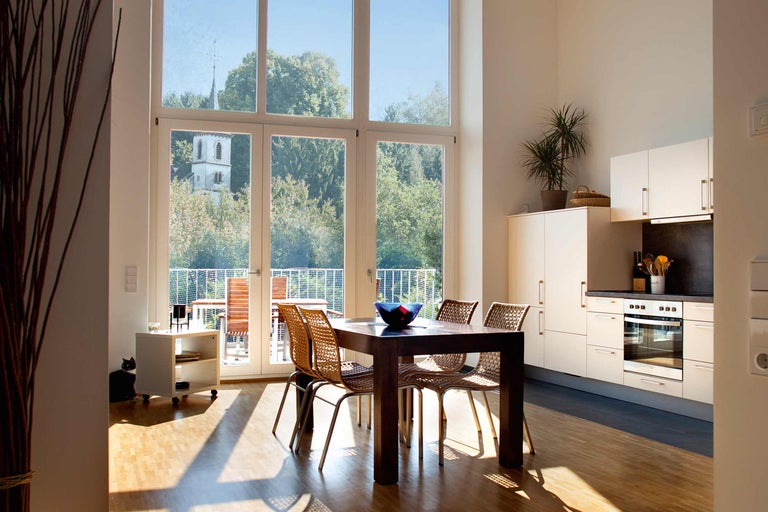 Heller Essbereich mit Esstisch, Stühlen, Küchenzeile und großem Fenster mit Blick ins Grüne