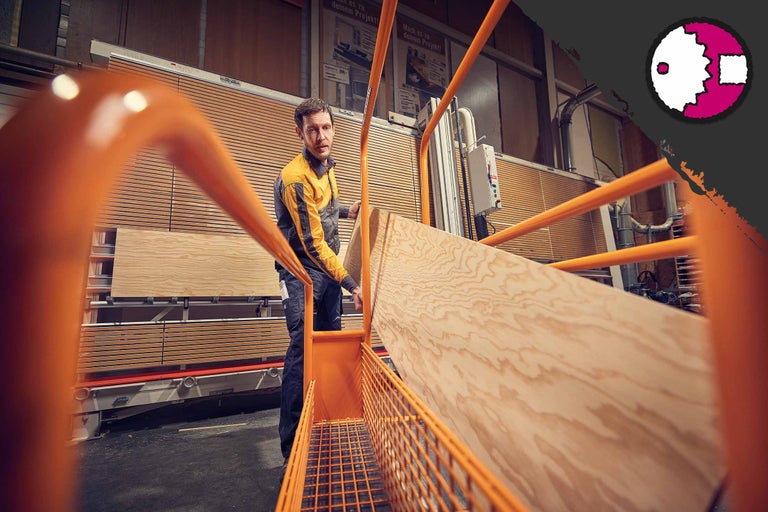Ein Mann hantiert mit einer Holzplatte in einer Werkstatt.