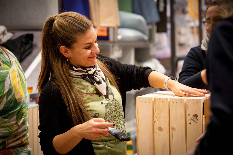Femme peignant une caisse en bois avec un pinceau.